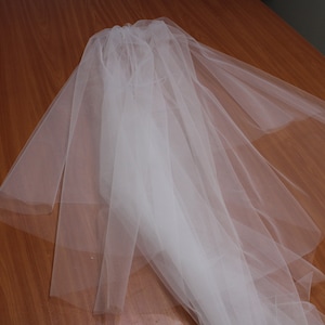 Puede incluir: Un velo de novia de tul blanco doblado sobre una superficie de madera.