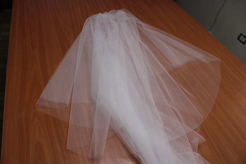 Puede incluir: Un velo de novia de tul blanco doblado sobre una superficie de madera.