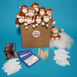 May include: A brown cardboard box filled with plush brown monkeys. The box has a label that says "Port-a-Pets". The monkeys are sitting on top of the box. There are also white fabric squares, wooden sticks, and gold stars on the blue surface.
