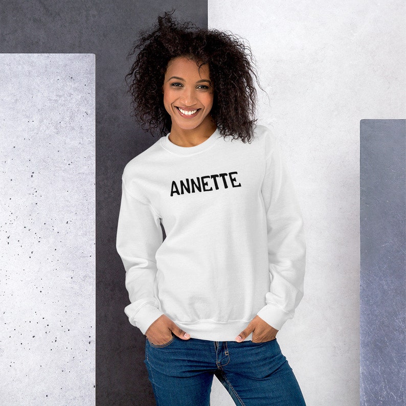 Op de afbeelding: Een wit sweatshirt met ronde hals met de naam "ANNETTE" in het zwart op de voorkant.