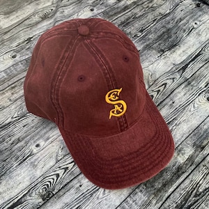 May include: A maroon baseball cap with a gold embroidered letter 'S' on the front.