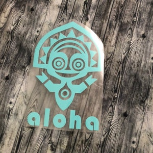 May include: A light blue vinyl decal with a cartoon tiki head and the word "Aloha" underneath. The decal is on a wood background.