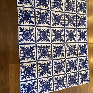 Puede incluir: Una colcha blanca y azul con un patr&oacute;n repetitivo de flores estilizadas. La colcha est&aacute; compuesta por cuadrados con un dise&ntilde;o de flores azules sobre un fondo blanco.