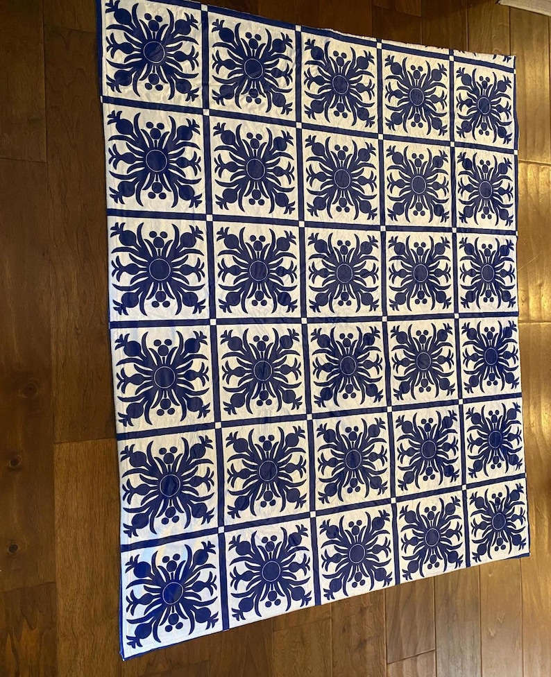 Puede incluir: Una colcha blanca y azul con un patr&oacute;n repetitivo de flores estilizadas. La colcha est&aacute; compuesta por cuadrados con un dise&ntilde;o de flores azules sobre un fondo blanco.