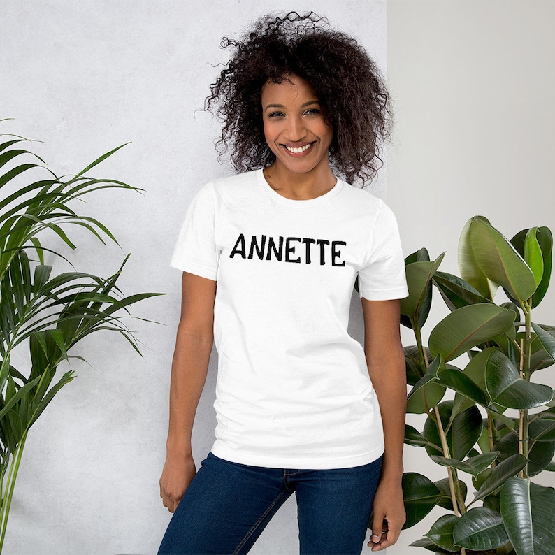 Puede incluir: Una camiseta blanca con la palabra "ANNETTE" impresa en negro en la parte delantera.