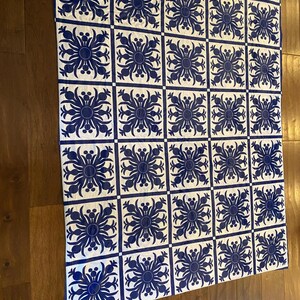 Puede incluir: Una colcha blanca con un patr&oacute;n repetitivo de dise&ntilde;os florales azules. La colcha est&aacute; compuesta por cuadrados con un dise&ntilde;o floral azul en cada cuadrado.