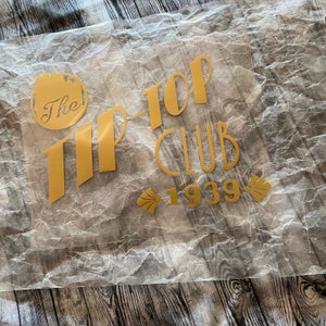May include: A gold vinyl sticker with the text "The Tip-Top Club 1939" on a white, crinkled background.