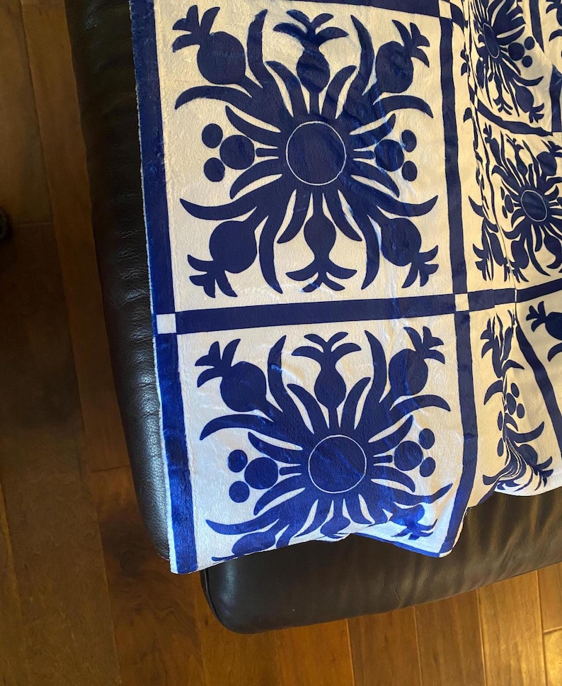 Puede incluir: Una tela con estampado blanco y azul con un dise&ntilde;o repetido de pi&ntilde;as y flores. La tela est&aacute; doblada y drapeada sobre una superficie de cuero marr&oacute;n.