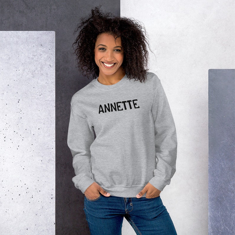 Op de afbeelding: Een grijs sweatshirt met het woord "ANNETTE" in zwart op de voorkant.