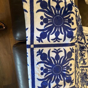 Puede incluir: Tela blanca con un patr&oacute;n floral azul. El patr&oacute;n es un dise&ntilde;o repetitivo de una flor estilizada con un c&iacute;rculo en el centro y hojas que irradian desde el centro. La tela es texturizada y tiene una superficie ligeramente elevada.