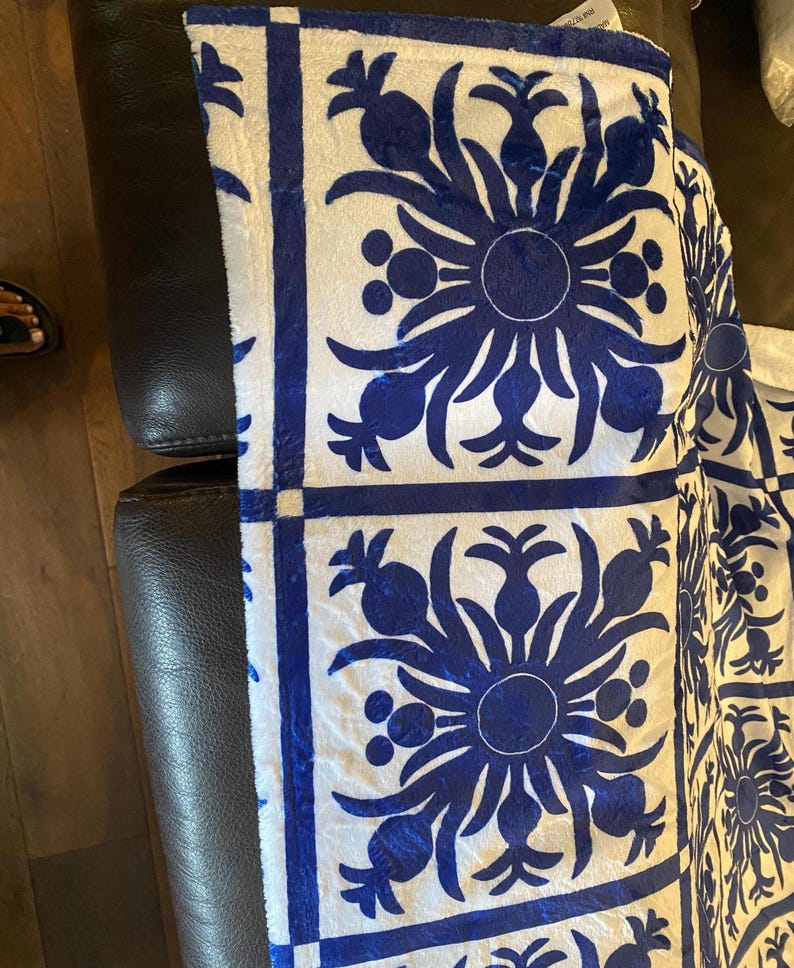 Puede incluir: Tela blanca con un patr&oacute;n floral azul. El patr&oacute;n es un dise&ntilde;o repetitivo de una flor estilizada con un c&iacute;rculo en el centro y hojas que irradian desde el centro. La tela es texturizada y tiene una superficie ligeramente elevada.