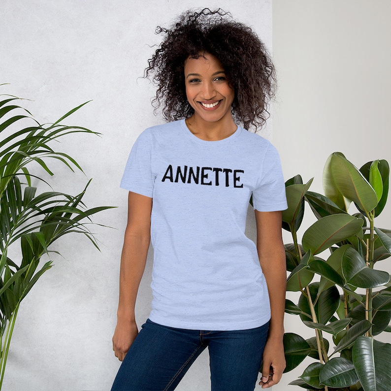 Puede incluir: Una camiseta azul claro con la palabra "ANNETTE" impresa en negro en la parte delantera.