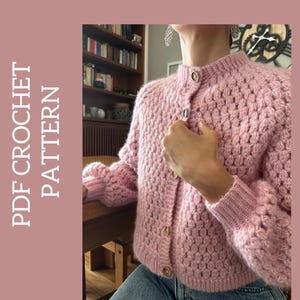 May include: A pink crocheted cardigan with a button fastening. The cardigan features a textured stitch pattern and is cropped in length.