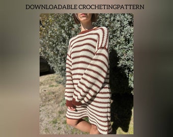 Può includere: Un abito a maglia all'uncinetto a righe marroni e bianche. L'abito ha una vestibilità ampia e maniche lunghe.