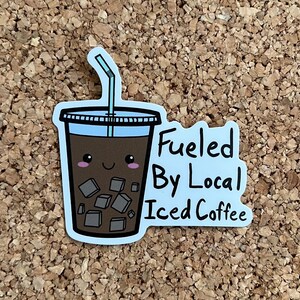 Könnte beinhalten: Ein blauer und weißer Aufkleber mit einem Cartoon-Eiskaffeebecher mit Strohhalm und dem Text "Fueled By Local Iced Coffee".