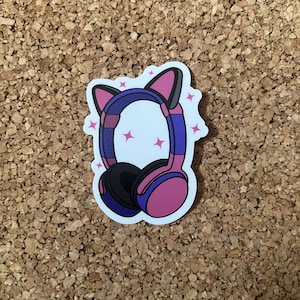 K&ouml;nnte beinhalten: Ein Aufkleber mit pinkfarbenen und blauen Kopfh&ouml;rern mit Katzenohren. Die Kopfh&ouml;rer haben einen wei&szlig;en Hintergrund mit pinkfarbenen Sternen.