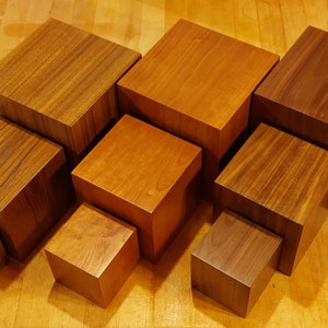 Op de afbeelding: Een set van zeven houten display-opstellingen in verschillende maten, van klein tot groot. De opstellingen zijn gemaakt van een rijk bruin hout met een natuurlijk houtnerfpatroon. Ze zijn in een verspringend patroon gerangschikt, waardoor een visueel aantrekkelijke weergave ontstaat.