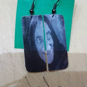 May include: A pair of black dangle earrings with a rectangular image of a woman's face. The image is in black and white and the woman is smiling.