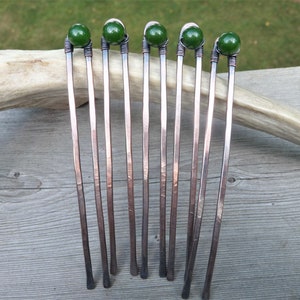 May include: Five U-shaped hair forks crafted from hammered copper wire, each featuring a single dark green spherical bead secured at the top with coiled wire detailing. The metal has a darkened, oxidized finish with visible texture.