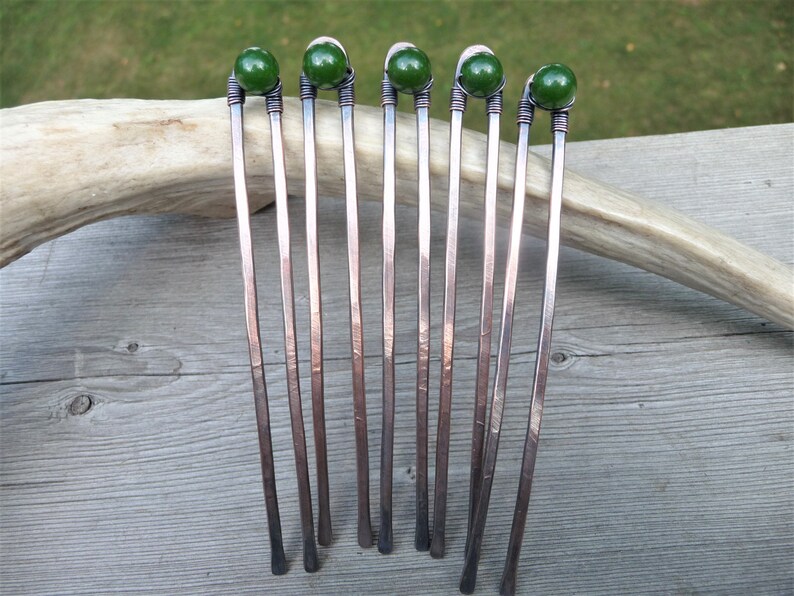 May include: Five U-shaped hair forks crafted from hammered copper wire, each featuring a single dark green spherical bead secured at the top with coiled wire detailing. The metal has a darkened, oxidized finish with visible texture.