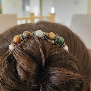 May include: A handcrafted hair accessory featuring a series of colorful, polished gemstones. The stones, in shades of brown, green, and blue, are intricately wired together. This unique hair piece is designed to be worn in the hair.