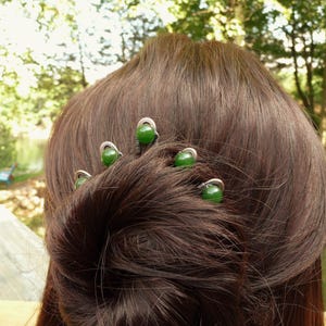 May include: A hair accessory featuring four silver-toned metal pins, each topped with a smooth, round, dark green bead. The pins are arranged in a curved formation, with each metal wire base wrapped around the bead to secure it in place.