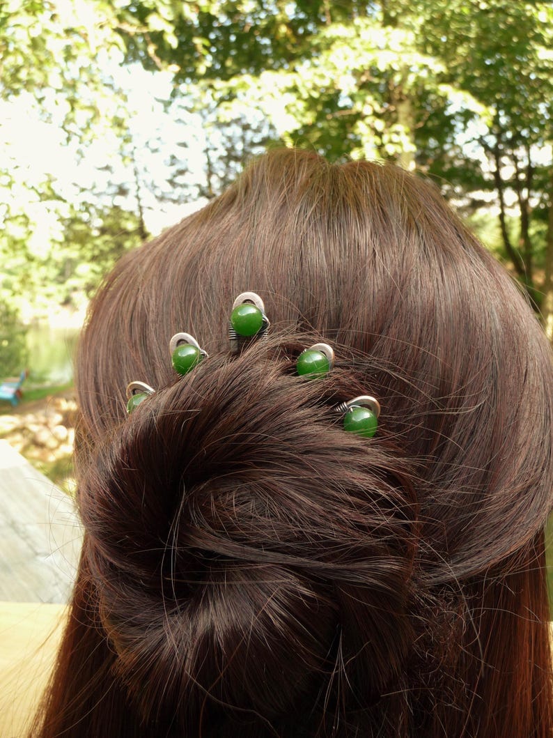 May include: A hair accessory featuring four silver-toned metal pins, each topped with a smooth, round, dark green bead. The pins are arranged in a curved formation, with each metal wire base wrapped around the bead to secure it in place.
