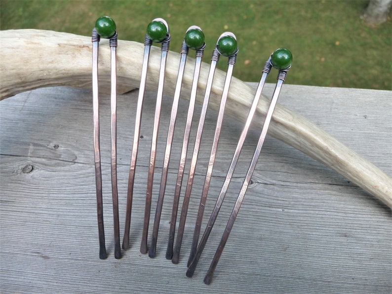 May include: Five U-shaped hair forks crafted from hammered copper wire. Each fork features two prongs and a single dark green spherical bead secured at the top with intricate wire wrapping. The metal has a warm, reddish-brown metallic finish.