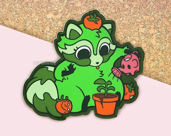 May include: A green raccoon illustration with a tomato on its head, watering a plant in a terracotta pot. The raccoon is holding a pink watering can. Additional tomatoes are scattered around the plant. The background is a glittery gold and pink.