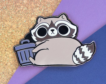 May include: A raccoon enamel pin with a trash can. The raccoon is light brown with a black mask and white accents. The trash can is gray. The pin has a gold outline and the text "PEN WINTER" in the bottom right corner.