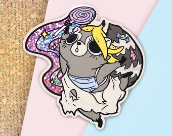 May include: A cartoon raccoon wearing a white dress with a blue trim and a yellow banana on its head. The raccoon is holding a pink and blue lollipop and is surrounded by pink and purple glitter.