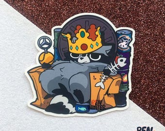 May include: A raccoon wearing a crown sits on a throne made of cans and other items. The raccoon is holding a fish bone in its paw. The throne is decorated with a wheel and a crown.