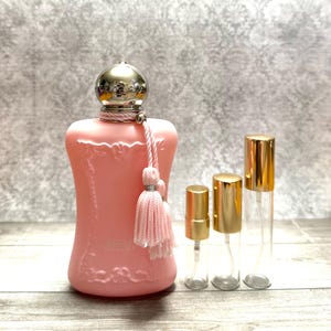 May include: A pink perfume bottle with a silver cap and a pink tassel, accompanied by three small, clear spray bottles with gold caps. The perfume bottle has an ornate design and the words "Delina Exclusif" are visible.