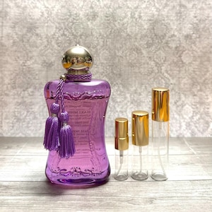 May include: A purple perfume bottle with a gold cap and matching tassels. Three clear glass spray bottles with gold caps are next to the perfume bottle. The perfume bottle has text on it.
