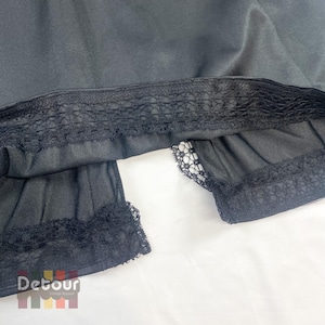 May include: Black vintage slip with lace trim. The slip has a detailed lace design along the hem and waistline. The fabric appears to be a smooth, opaque material. The brand name "Detour Vintage Apparel" is visible in the bottom left corner.