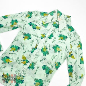 May include: A light green long-sleeved shirt with a repeating pattern of green grapes and the text "Win Grape" printed on it.