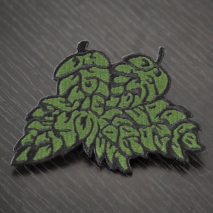 May include: Green embroidered patch shaped like a cluster of hops. The patch is made of fabric and has a black outline.