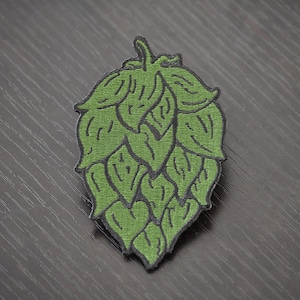 May include: Green embroidered hop cone patch. The patch is detailed with black stitching and has a realistic design.