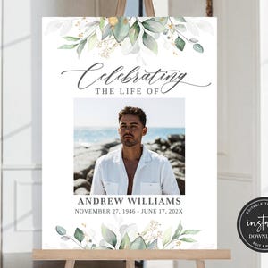 May include: A white sign with a green and white floral design at the top and bottom. The sign says "Celebrating the life of" and has a photo of a man in the middle. The text below the photo says "Andrew Williams November 27, 1946 - June 17, 202X".