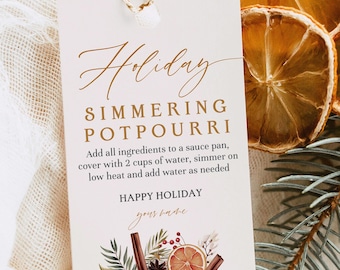 May include: A rectangular white paper tag with a gold string, featuring the text Holiday SIMMERING POTPOURRI, instructions to add ingredients to a sauce pan with 2 cups of water, and a graphic of dried orange slices, cinnamon sticks, and pine.