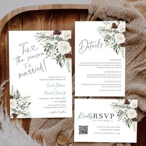 May include: A wedding invitation suite featuring three white cards with floral accents of white roses, pine cones, and evergreen sprigs. The text includes 'Tis the season to be married!', 'Details', and 'Kindly RSVP' with a QR code included.
