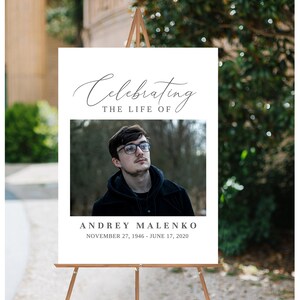 K&ouml;nnte beinhalten: Ein wei&szlig;es Schild mit schwarzem Text, auf dem steht "Celebrating the Life of Andrey Malenko November 27, 1946 - June 17, 2020". In der Mitte des Schildes ist ein Foto eines Mannes mit Brille.