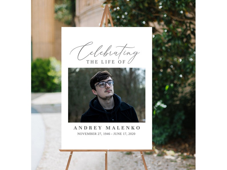 K&ouml;nnte beinhalten: Ein wei&szlig;es Schild mit schwarzem Text, auf dem steht "Celebrating the Life of Andrey Malenko November 27, 1946 - June 17, 2020". In der Mitte des Schildes ist ein Foto eines Mannes mit Brille.