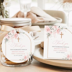 May include: A glass jar with a silver lid and a cream-colored ribbon, holding cookies. A round tag and a square card feature floral designs, a cross, and the text "Thank you" for a First Communion.