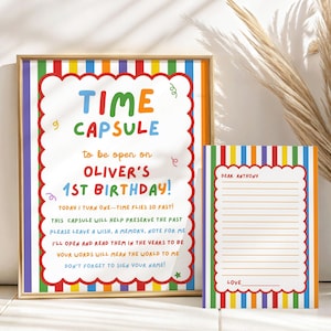 Pode incluir: Uma placa emoldurada e um cartão a condizer com uma borda de riscas verticais coloridas e uma moldura vermelha recortada. A placa diz TIME CAPSULE to be open on OLIVER'S 1ST BIRTHDAY com texto adicional. O cartão tem linhas para escrever.