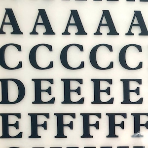 May include: A sheet of black adhesive letters on a white background. The letters are in uppercase and include the alphabet from A to O.