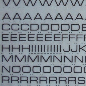 May include: A sheet of Letraset instant lettering in black on a white background. The sheet contains the alphabet in uppercase, numbers, and punctuation marks. The sheet is labeled "Letraset instant lettering" and "MICROGRAMMA MEDIUM EXTENDED".