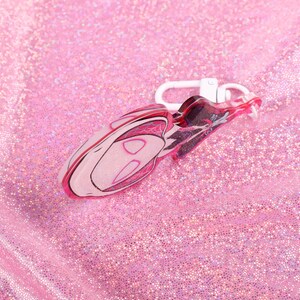 May include: Pink and white plastic keychain shaped like a cartoon character with a white metal clasp.