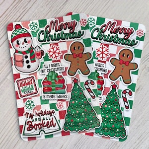 May include: Two Christmas-themed stickers with a red and green checkered background. One sticker features a snowman, and the other has a gingerbread man. Text includes "Merry Christmas", "All I want for Christmas", "My holidays are all booked", and "Holly Jolly Vibes".