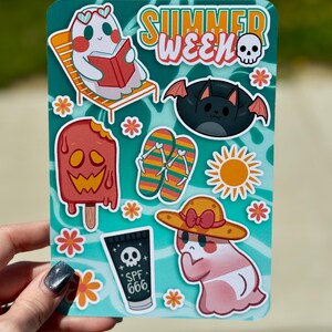 May include: A sticker sheet with a teal background featuring summer-themed illustrations. Includes a ghost reading a book, a bat, a melting popsicle, flip-flops, a sun, and a ghost wearing a hat. The text "SUMMER WEEK" and "SPF 666" are also present.